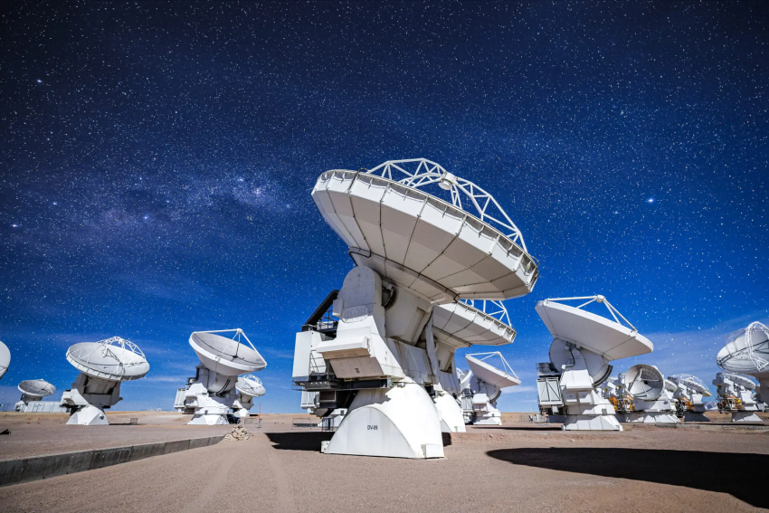 ALMA's DV-59 antenna in the foreground with multiple other antennas observing the sky in a night dominated by the Moon.