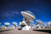 ALMA's DV-59 antenna in the foreground with multiple other antennas observing the sky in a night dominated by the Moon.